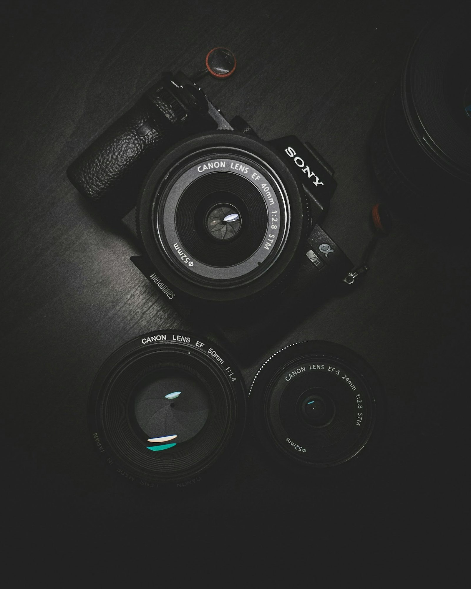Macchina fotografica nera e tre obiettivi appoggiati su un tavolo scuro.